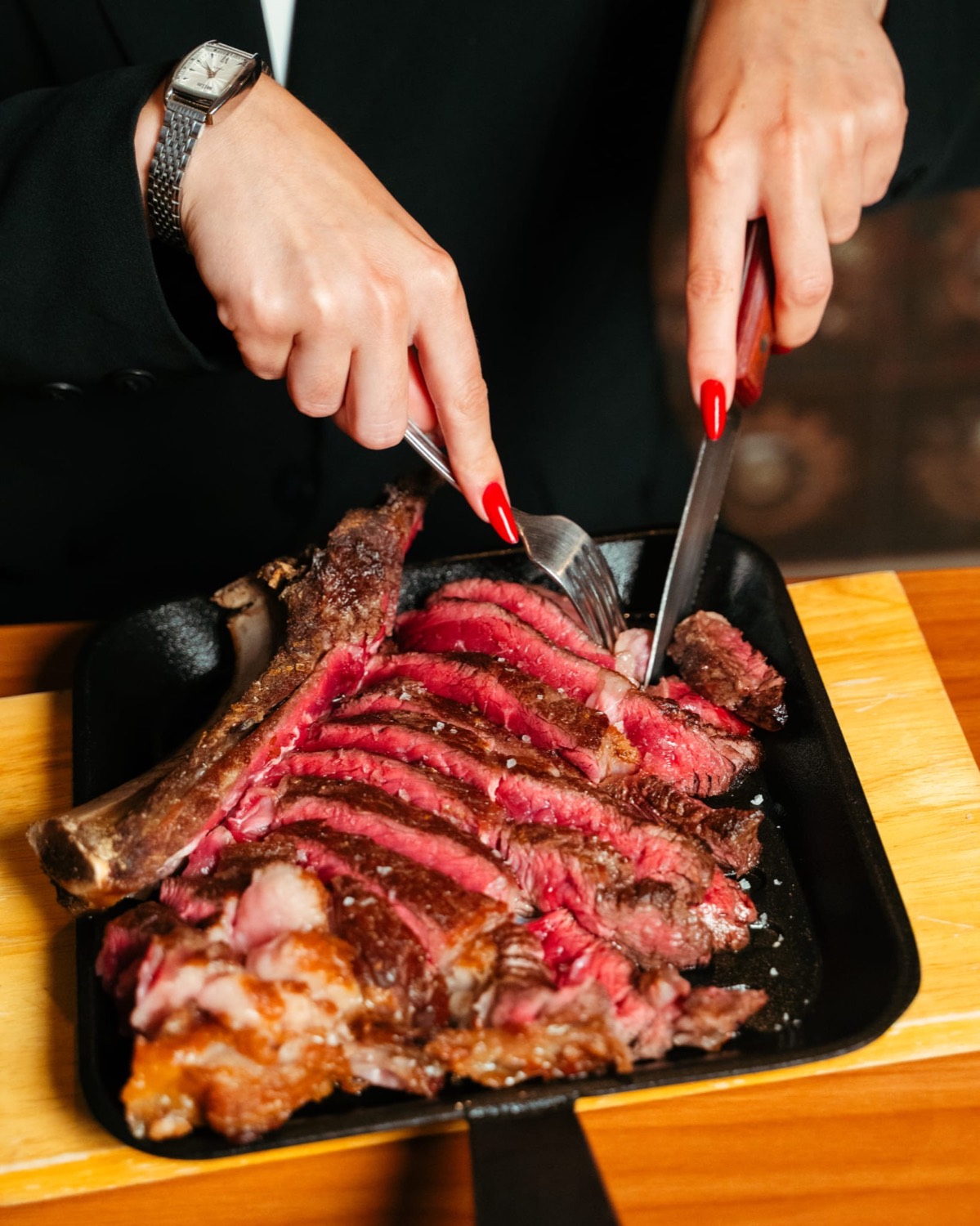 Mani che tagliano la tagliata in padella di ghisa al tavolo — Domas Steakhouse
